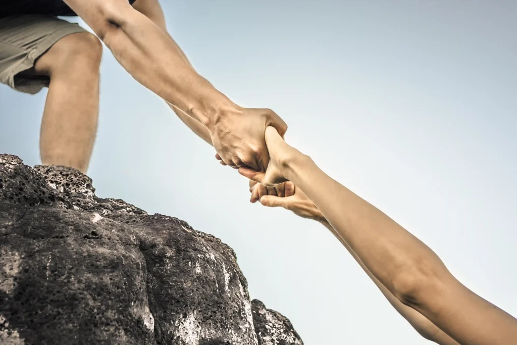 A person on a rock mount pushing someone up by the hand